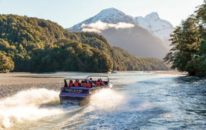 Jet boat travelling up river towards snowy mountain 