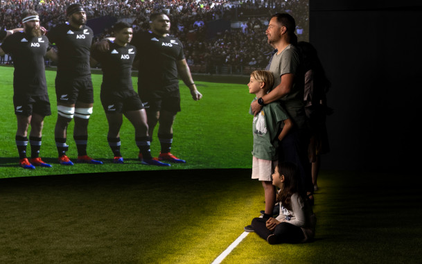 Man standing with son in front of All Blacks on big screen