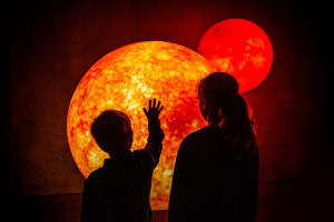 Two children standing in front of model of glowing planet
