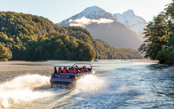 Jet boat travelling up river towards snowy mountain 