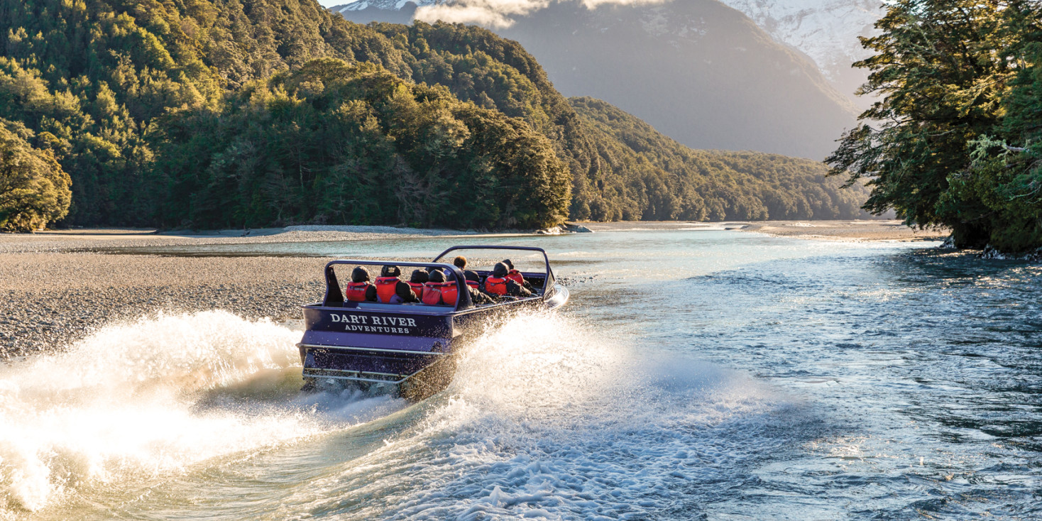 Jet boat travelling up river towards snowy mountain 