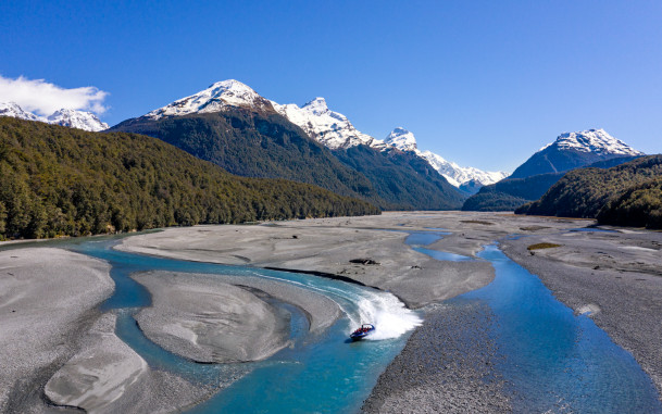 Jetboat travelling up braided riverbed with snowcapped mountains in surrounds