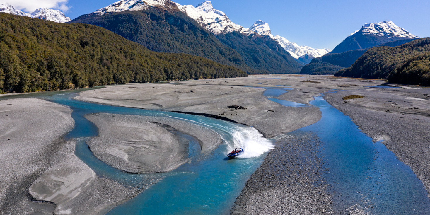 Jetboat travelling up braided riverbed with snowcapped mountains in surrounds