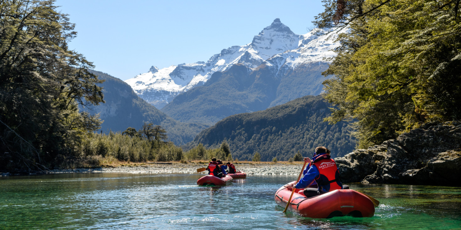 Pair of inflatable canoes paddling towards a snowcapped mountain 
