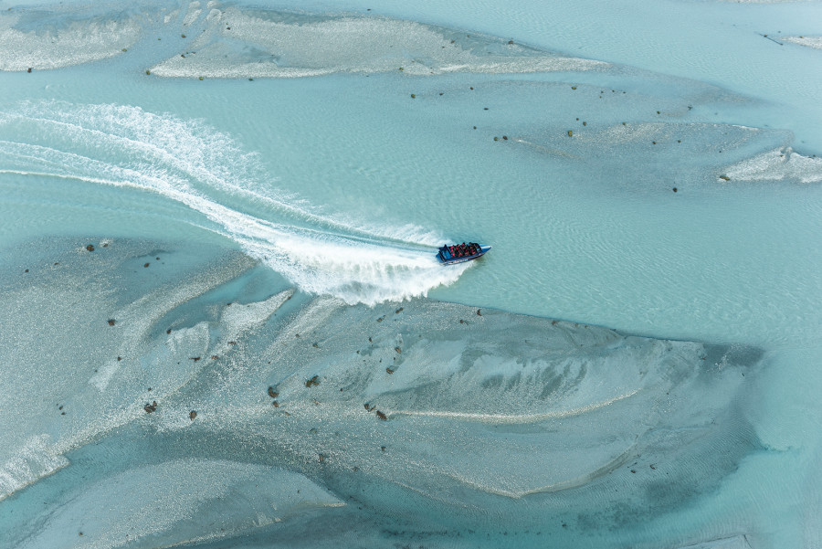 Aerial view of jetboat driving down river with wake behind it