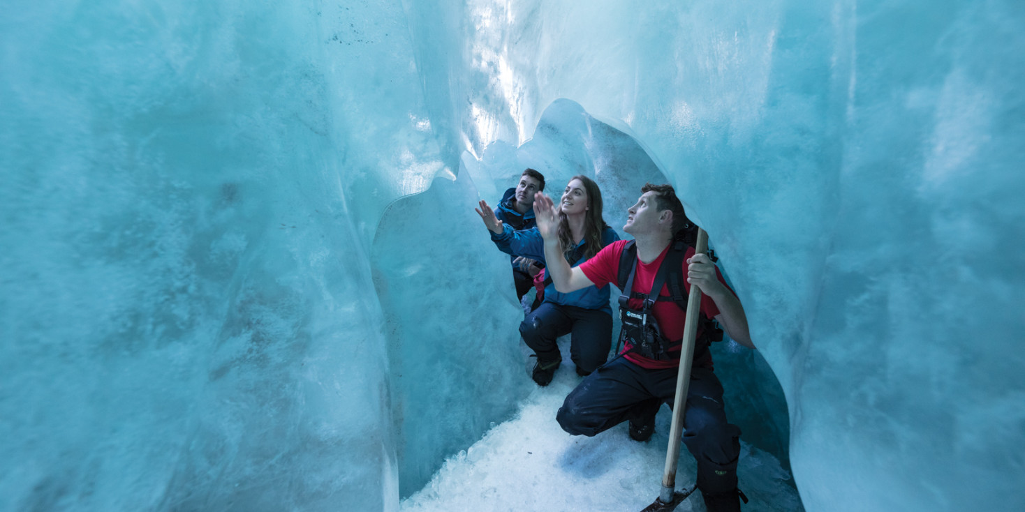 Group huddling together underneath large block of ice on glacier
