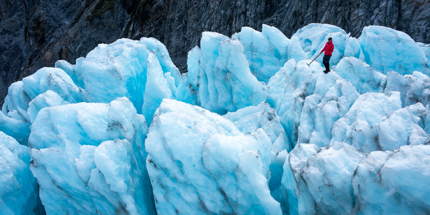 Person standing on light blue glacier with ice axe in hand