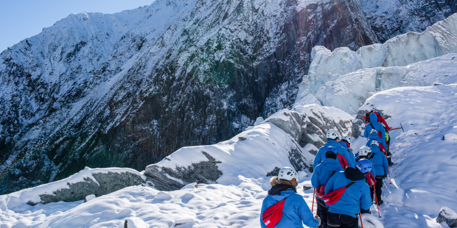 Group hiking up the side of glacier towards sun peaking over mountain range