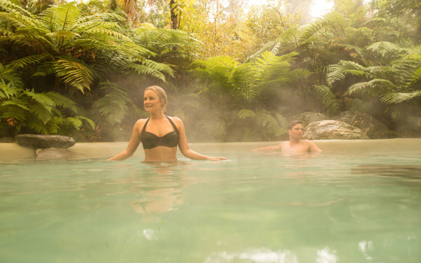Couple relaxing in the steam of large hot pool with surrounding native plants