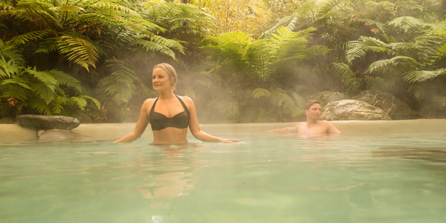 Couple relaxing in the steam of large hot pool with surrounding native plants