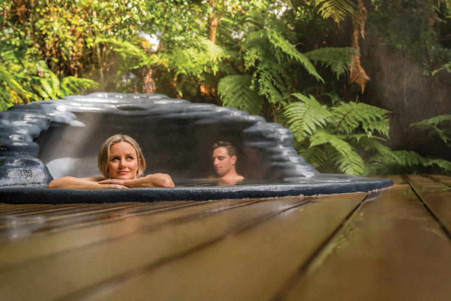 Couple relaxing in natural hot pool surrrounded by native bush