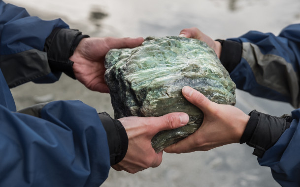 Two sets of hands holding large greenstone rock