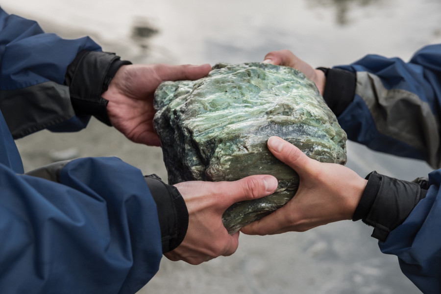Two sets of hands holding large greenstone rock