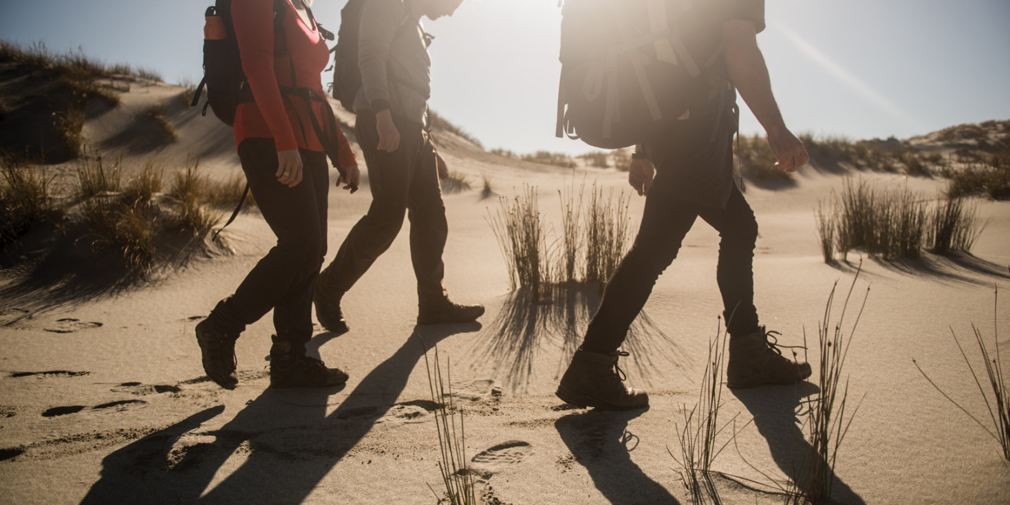 Group of three hikers walking along beach with sun in the background