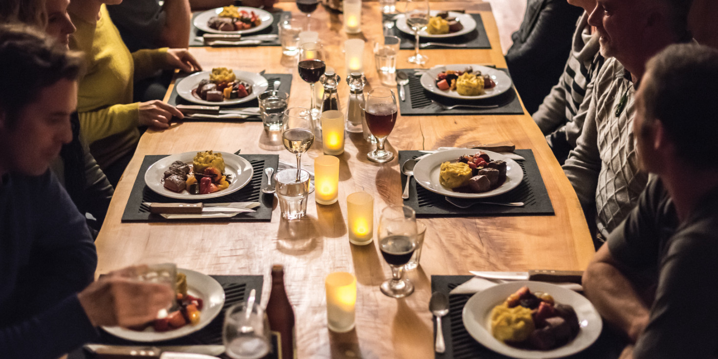 Group of people sitting at dinner table with food and drinks