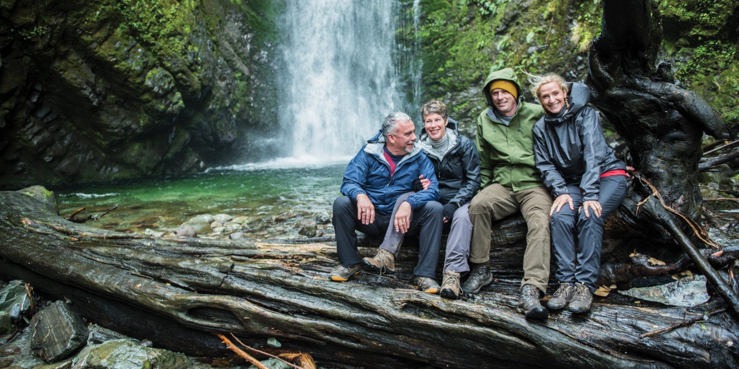 Group sitting on fallen tree in front of waterfall