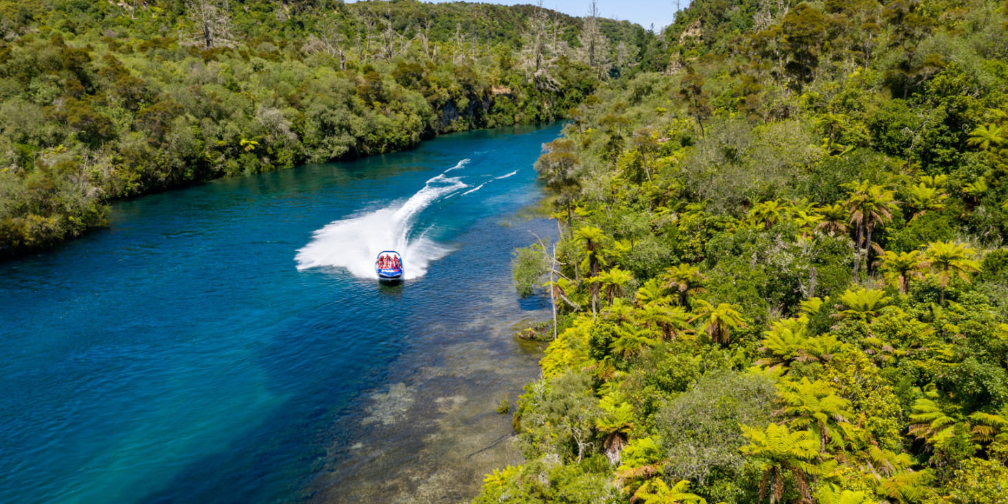 Wide shot of jet boat travelling down pristine river lined by bush