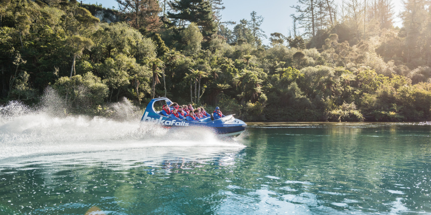Jet boat racing down river with native bush in background 
