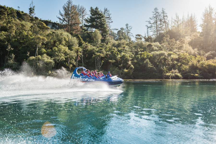 Jet boat racing down river with native bush in background 