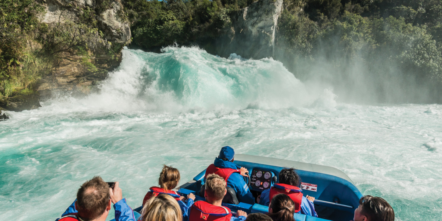 Passengers on jet boat admiring powerful waterfall 