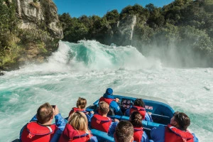 Passengers on jet boat admiring powerful waterfall 