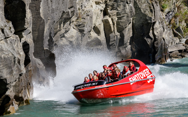 Jet boat speeds along river towards rocky cliff face