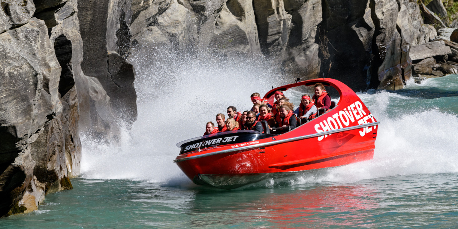 Jet boat speeds along river towards rocky cliff face