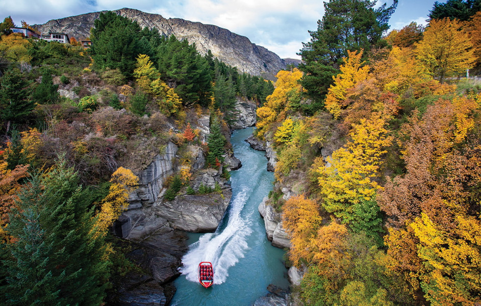 Jet boat driving down narrow canyon with autumn trees either side
