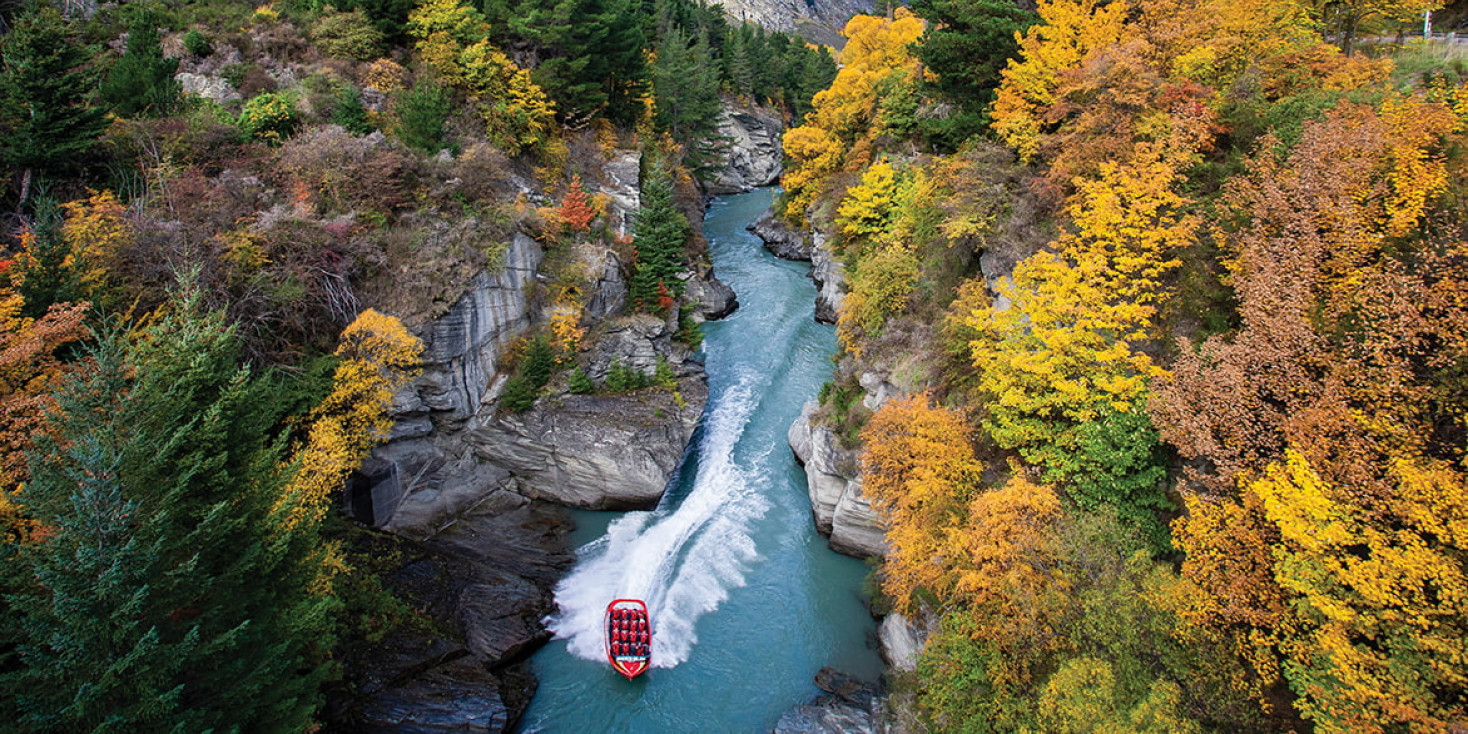 Jet boat driving down narrow canyon with autumn trees either side